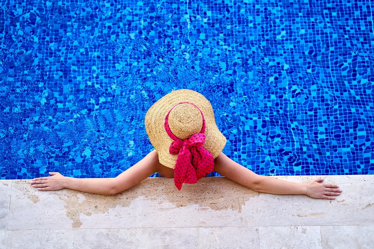 Aerial view of a woman relaxing in a custom pool with a beach hat, highlighting a serene wellness‑focused backyard setting.